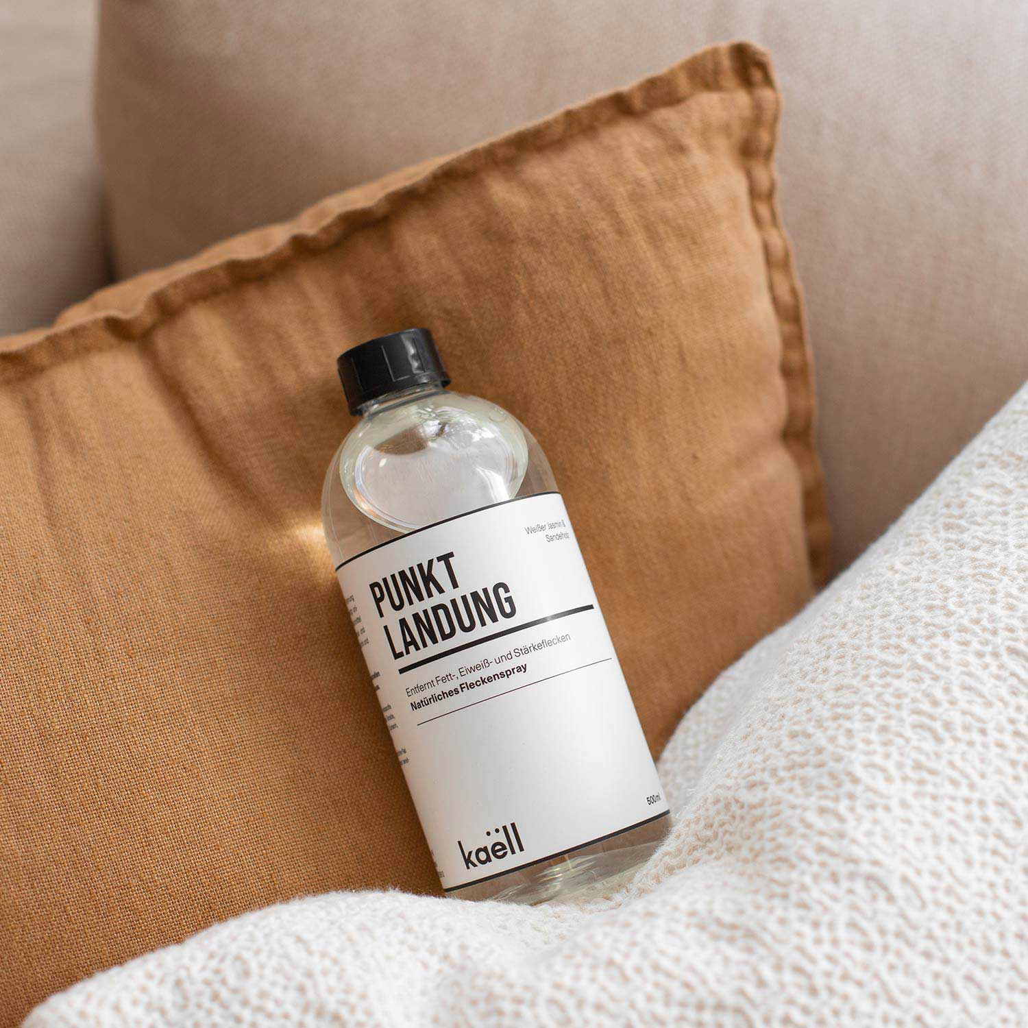 Eine Flasche mit der Aufschrift 'Punktlandung', liegt dekorativ auf einem braunen Kissen. Im Hintergrund ist ein weiß strukturiertes Kissen zu sehen. Oben links im Bild befindet sich ein orangefarbenes Feld mit dem Schriftzug 'NEU'.