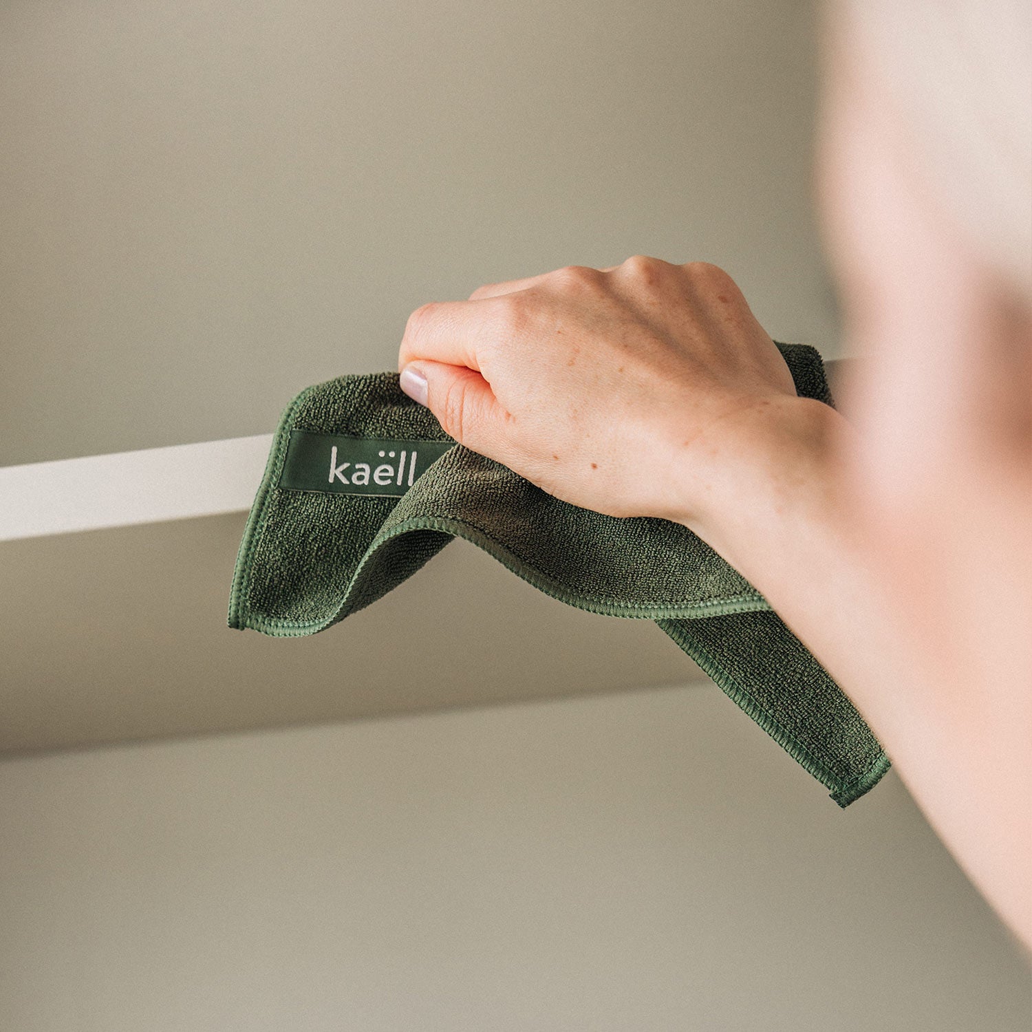 Eine Hand wischt eine Oberfläche mit einem grünem antibakteriellem Mikrofasertuch.